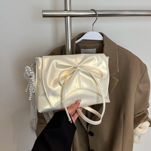 Détail du sac blanc nacré avec grand nœud, bordure en dentelle et breloque perle