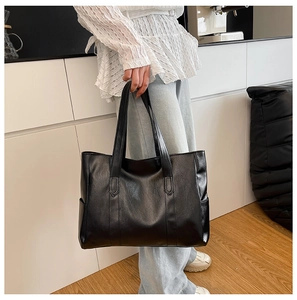 Detailed view of black faux leather tote bag with side pockets in a modern interior setting