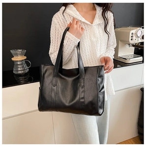 Detail showing the large black leather tote bag with side pockets and wide handles