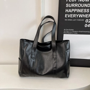 Λεπτομέρεια μαύρης τσάντας tote με ανάγλυφη υφή δέρματος και πρακτική πλαϊνή θήκη αποθήκευσης