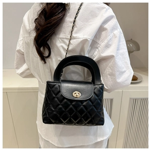Detail of black quilted leather crossbody bag with gold hardware on a white shirt