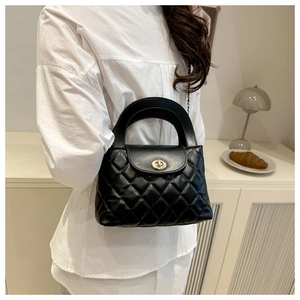 Detail of black quilted leather handbag with gold twist lock and chain strap on shoulder