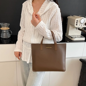 Bolso tote de cuero marrón con letras doradas en una elegante escena de cafetería