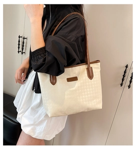Detail of houndstooth embossed fabric and brown leather strap on cream tote bag