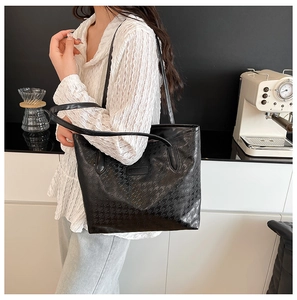 Close-up of a black tote bag featuring textured houndstooth patterns and leather straps