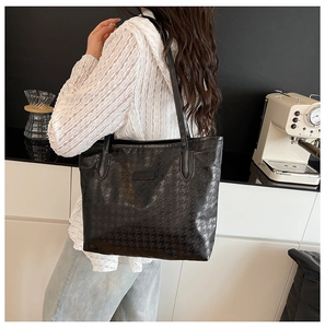 Detail of black houndstooth embossed tote bag with glossy finish and slim shoulder strap