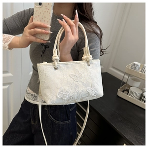Detailed view of white lace handbag featuring elegant butterfly embroidery and knot handles