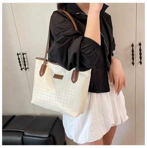 Detail of large houndstooth tote bag with brown leather handles worn by a model