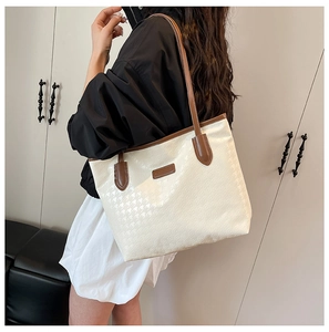 Detail view of large houndstooth tote bag with brown leather handles on a model
