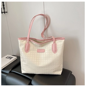 Detail of houndstooth tote bag with pink straps and brand tag on a leather stool