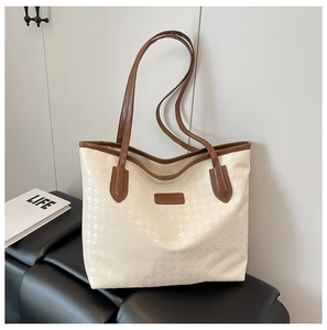 Detail of houndstooth embossed texture and brown leather trim on the beige tote bag
