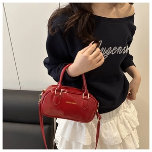 Gros plan du mini sac Boston en cuir verni rouge avec logo doré et bandoulière