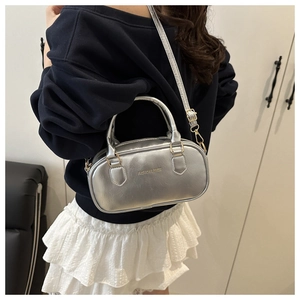 Silver mini bowling bag worn crossbody by a model with a dark blue shirt and white skirt