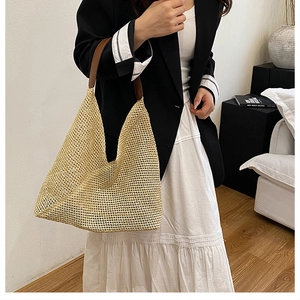 Detail of hand-woven straw hobo bag featuring dark brown leather handle and natural texture