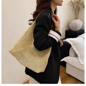 Close-up of a large woven straw tote bag featuring brown leather straps on a model