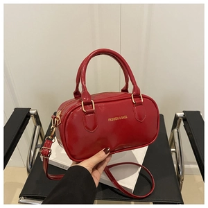 Détail du sac bowling en cuir verni rouge avec finitions dorées et slogan de mode