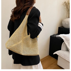 Close-up of beige woven straw tote bag with brown faux leather strap worn by a model