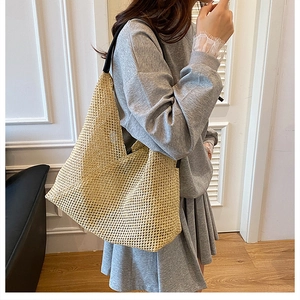 Detailed view of beige hand-woven straw tote bag with black shoulder straps on model