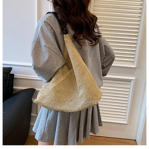 Detail shot of a beige woven straw shoulder bag with black strap on a female model