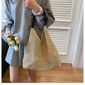 Detail of woven straw tote bag texture with black shoulder strap and hollow mesh pattern