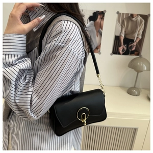 Close-up of black crossbody bag with gold round lock and chain detail on modern background