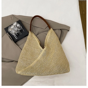 Macro view of woven straw beach bag featuring brown leather shoulder strap and mesh texture