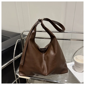 Detail of coffee brown hobo bag with retro leather grain and adjustable strap on a glass shelf