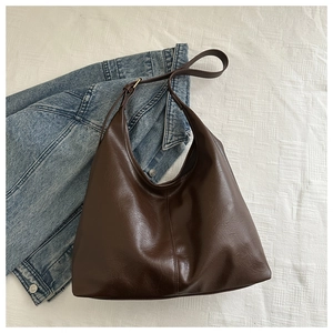 Detail of dark brown leather bucket bag with adjustable metal buckle on textured fabric