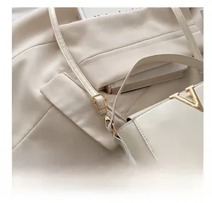 Detail of adjustable leather strap and golden V-shaped logo on cream crossbody bag
