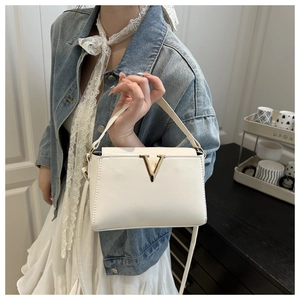 Detail shot of a white patent leather handbag with a gold V-shaped metal buckle clasp