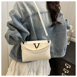 Detail of white patent leather crossbody bag with golden V-shaped buckle on denim outfit