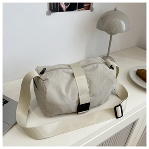 Detail of beige nylon crossbody bag with adjustable strap and buckle on a minimalist desk