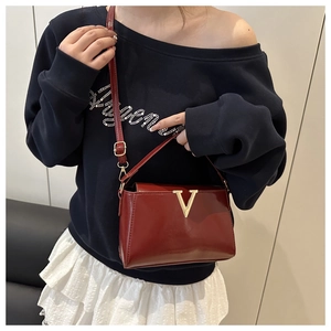 Detail of burgundy glossy leather square bag with large gold V buckle and detachable strap