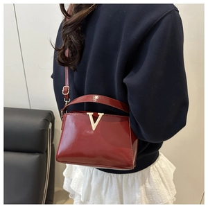 Burgundy patent leather handbag with gold V-buckle worn by a model in a modern interior
