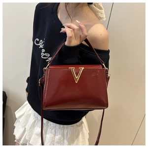 Detailed macro view of glossy burgundy patent leather handbag with gold metal V-buckle