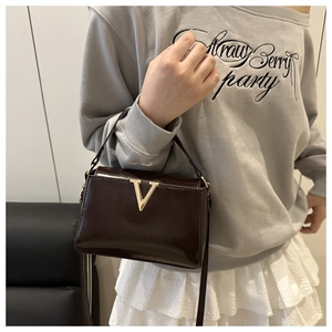 Detail of dark brown patent leather handbag with gold V-shaped metal hardware and strap