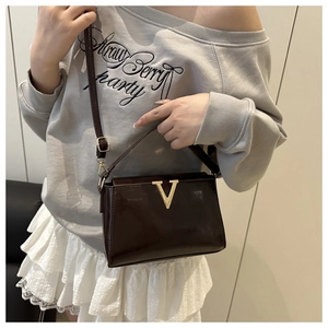 Detail of a luxury dark brown polished shoulder bag with a gold V-shaped metal buckle