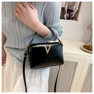 Detail of a chic black square handbag with a gold V-shaped buckle and a slim shoulder strap