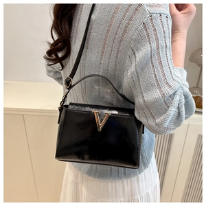Detail of glossy black leather crossbody bag with gold metal V logo shown on a model