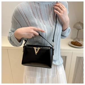 Detail showing elegant black patent leather shoulder bag with golden V-shaped buckle