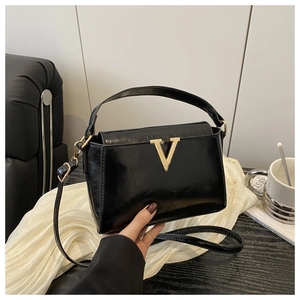 Detail of elegant black glossy patent leather handbag with golden V-shaped buckle