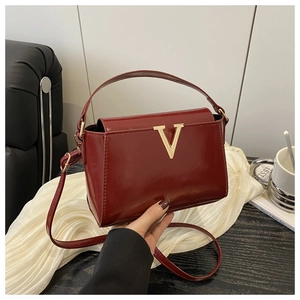 Close-up of glossy wine red patent leather handbag with a gold V-shaped buckle detail