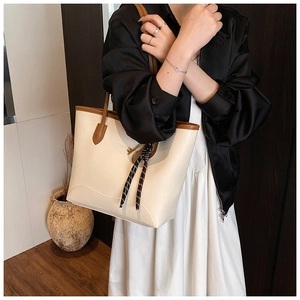 Detail of cream tote bag with litchi texture and brown straps worn by a model