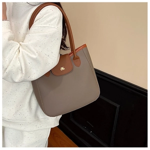 Détail du sac cabas taupe avec bordure marron et logo métallique doré porté à l'épaule