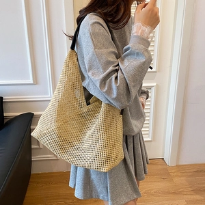Beige hand-woven tote bag with dark leather shoulder straps shown in a minimalist setting