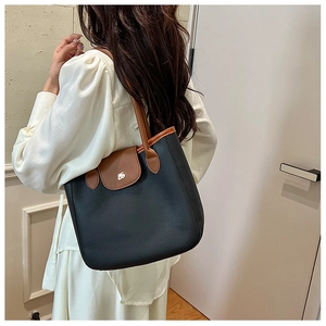 Détail d'un sac cabas bicolore en cuir grainé noir avec poignées marron et logo doré chic