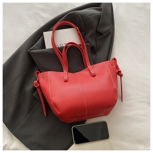 Detail of red leather tote bag featuring white stitching and drawstring side knots