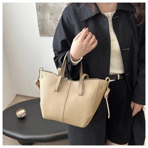 Detail of beige litchi grain leather tote bag with wing-shaped sides and decorative knots