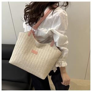 Dettaglio borsa tote in paglia intrecciata con tracolla rosa e toppa Fashion sulla spalla