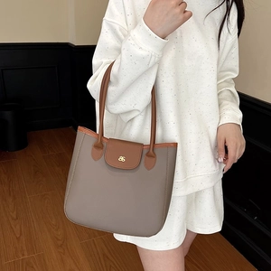 Sac cabas bicolore gris et marron avec logo doré porté par un mannequin chic